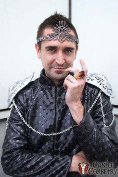 a man dressed in black and silver holding a piece of food up to his mouth