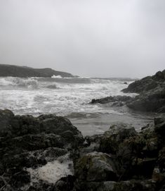 the water is crashing over the rocks at the beach on a foggy, cloudy day