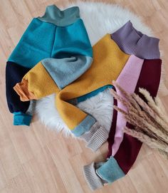 several different colored sweaters laying on top of a white furnishing area next to a dried plant