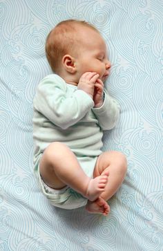 a baby laying on top of a bed with his hands in his mouth and eyes closed