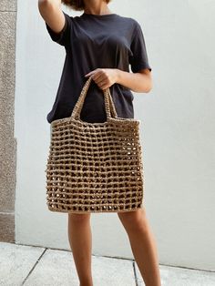 a woman in black shirt and brown shoes holding a beige handbag with holes on it