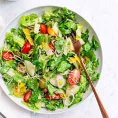 a white plate topped with a salad next to a fork and bowl filled with dressing