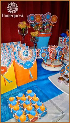 an assortment of desserts displayed on a table with blue and orange decorations in the background