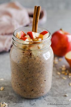 an apple pie in a glass jar with cinnamon stick sticking out of the top and apples on the side