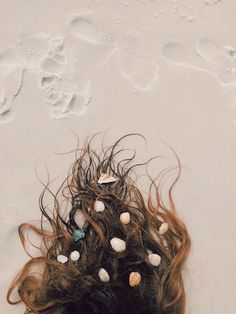 an overhead view of a woman's head on the beach with seashells in her hair