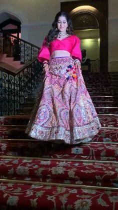 a woman in a pink top and skirt walking down some red carpeted staircases