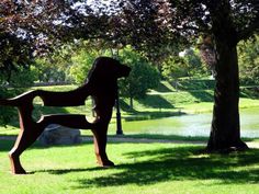 a statue of a dog in the middle of a grassy area next to a tree