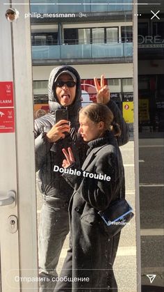 two people standing in front of a door with their hands up and one person making the peace sign