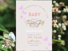 a pink and gold baby shower is displayed next to some white flowers on a green plant