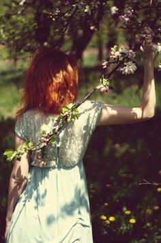 a woman in a blue dress is walking through the woods with flowers on her back