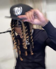 a person with dreadlocks holding a baseball cap over their head and pointing to the side