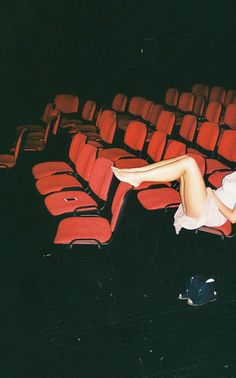 a woman laying on top of a red chair in front of an empty theater seat