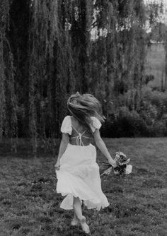 a woman in a white dress is walking through the grass with her hair blowing in the wind