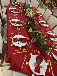 the table is set for christmas dinner with red linens and gold place settings, including silverware