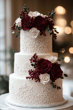 a three tiered wedding cake with red and white flowers on the top, sitting on a table