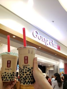 two people holding up drinks in front of a sign that says gong chua on it