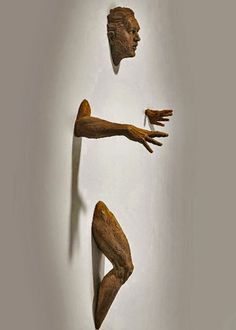 three wooden sculptures in the shape of hands and legs, hanging on a white wall