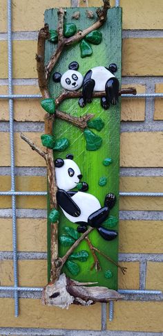 two pandas are sitting on the tree branch in front of a wall with green leaves