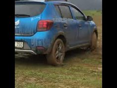 a blue car driving down a dirt road next to a green grass covered field on a cloudy day