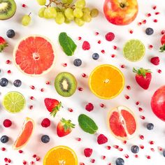 various fruits and vegetables are arranged on a white surface with red berries, oranges, kiwis, grapes, strawberries