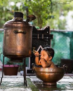 a small child in a bowl playing with water from a faucet on the ground