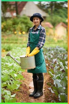 a woman in an apron and rubber boots is holding a watering can while standing in a garden