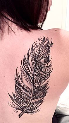 the back of a woman's shoulder with a feather tattoo on her left side