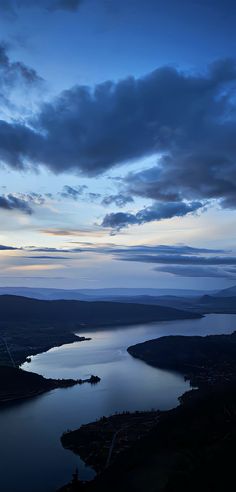 the sky is very dark and cloudy at dusk over a large body of water with mountains in the distance