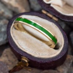 an open ring with a green stripe on it sitting in a box next to some rocks