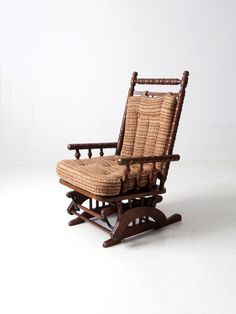 an old rocking chair with a cushion on the back and seat is sitting in front of a white wall