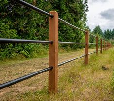 a wooden and metal fence on the side of a dirt road in front of trees