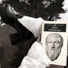 a person wearing white socks and black shoes holding a book in their left hand with an image of a bust on it