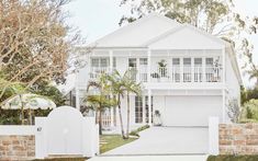 a large white house with palm trees in the front yard and gated driveway area