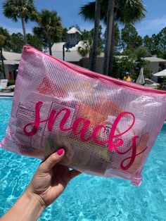 a person holding up a pink bag near a swimming pool with palm trees in the background