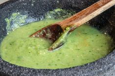 a wooden spoon in a black bowl filled with green liquid