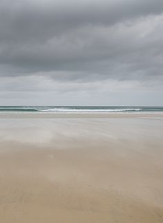 an empty beach with waves coming in to the shore and dark clouds above it on a gloomy day