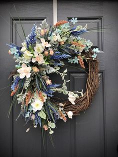 a wreath with flowers and greenery hanging on the front door to welcome people into the house