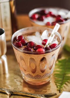 two glasses filled with ice and cranberries on top of a table next to silverware