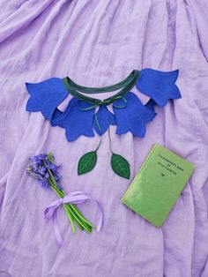 a book and some flowers are laying on a purple sheet with a ribbon around it