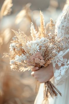 a woman in a white dress holding a bouquet of wildflowers and wheat stalks