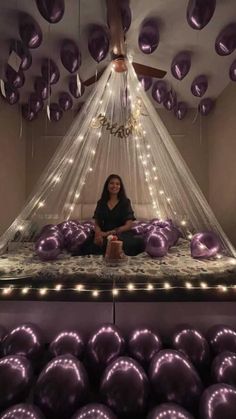 a woman sitting on top of a bed surrounded by purple balloons and lights in the ceiling