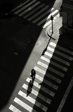 an aerial view of a person walking across a crosswalk in the middle of a city