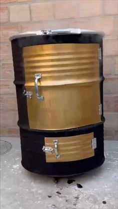 a large black and gold drum sitting on top of a cement floor next to a brick wall