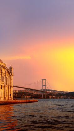 the sun is setting over an old building by the water with a bridge in the background