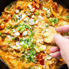 a hand is picking up some food from a skillet with cheese and green onions