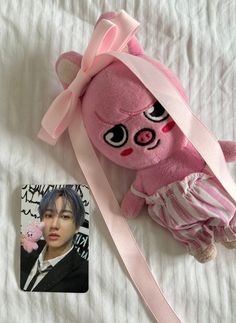 a pink teddy bear with big eyes laying on a bed next to a small photo