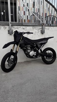 a black motorcycle parked in front of a white wall and some stairs on the other side