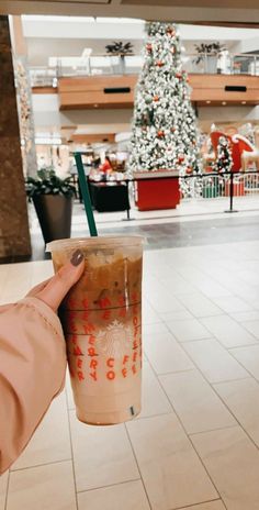 a person holding up a drink in front of a christmas tree at an airport terminal