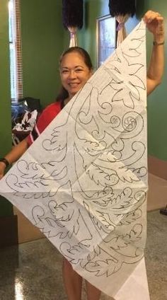 a woman holding up a white kite with black designs on it's sides and smiling at the camera