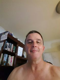 a shirtless man standing in front of a bookshelf with his eyes closed